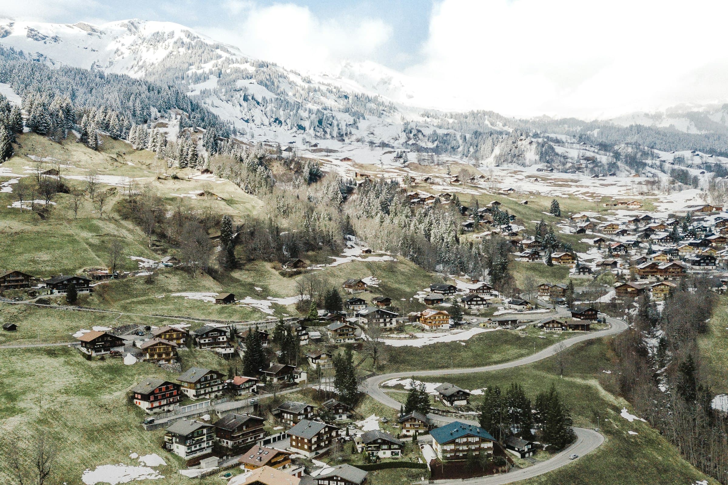 Aerial view of a Swiss mountain town, houses spread across a valley beneath high peaks